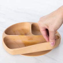 Load image into Gallery viewer, A hand holds a Bumkins Silicone Grip Dish: Wood Grain, demonstrating the suction cup bottom on a marble surface.
