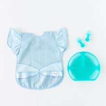 Load image into Gallery viewer, Bumkins Ruffle Apron Bib: Cinderella rests next to a blue divided plate and blue toddler utensils on a white background.

