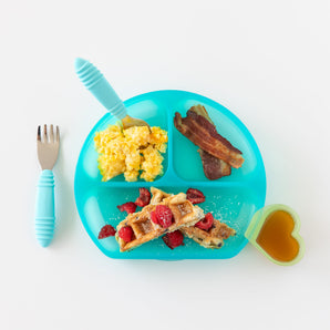 Bumkins Silicone Grip Dish: Blue Jelly with eggs, bacon, and waffles, a heart-shaped cup of syrup, and blue utensils on a white background.