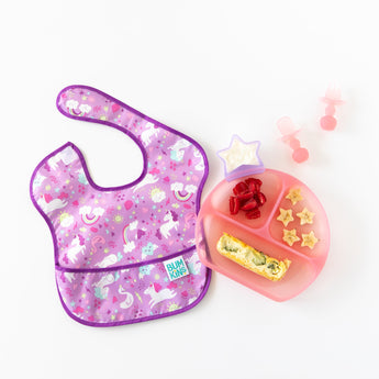 Bumkins Silicone Grip Dish: Pink Jelly with breakfast foods sits next to matching toddler utensils and a purple bib on a white background.