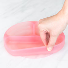 Load image into Gallery viewer, A hand holds a Bumkins Silicone Grip Dish: Pink Jelly, demonstrating the suction cup bottom on a marble surface.
