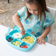Load image into Gallery viewer, A child enjoys breakfast from a Bumkins Silicone Grip Dish with Lid (5 Section): Blue with a spoon at a white table while wearing a blue bib.
