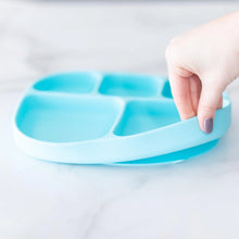 Load image into Gallery viewer, A hand holds a Bumkins Silicone Grip Dish with Lid (5 Section): Blue, demonstrating the suction cup bottom on a marble surface.

