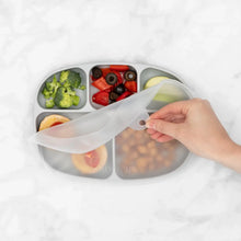 Load image into Gallery viewer, A hand removes the lid from Bumkins Silicone Grip Dish with Lid (5 Section): Gray filled with veggies and more on a marble surface.

