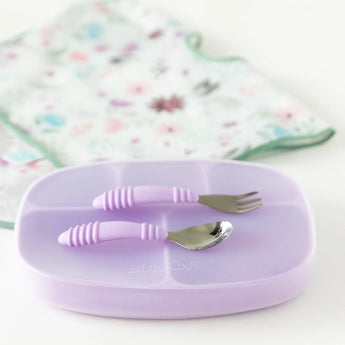 Bumkins Silicone Grip Dish with Lid (5 Section): Lavender sits on a white background with utensils on top, and a floral bib in the backdrop.
