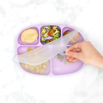 A hand lifts the lid from a Bumkins Silicone Grip Dish with Lid (5 Section): Lavender filled with veggies and more on a marble background.