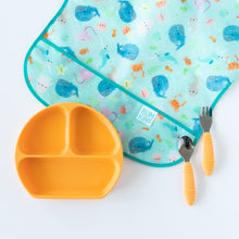 Load image into Gallery viewer, Bumkins Silicone Grip Dish: Tangerine rests on a white background among a whale print bib and orange utensils.
