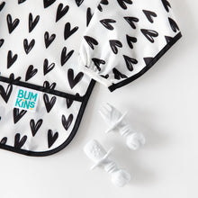 Load image into Gallery viewer, Close-up of Bumkins Silicone Chewtensils®: Marble next to a black &amp; white heart-patterned sleeved bib on a white background.
