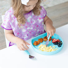 Load image into Gallery viewer, A child in a purple bib enjoys eggs, potatoes, and fruit from a Bumkins Silicone Grip Plate: Blue with a fork on a white table.
