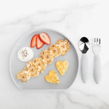 Load image into Gallery viewer, Bumkins Silicone Grip Plate: Gray holds banana, oats, yogurt, berries, &amp; heart-shaped waffles beside gray utensils on a marble background.
