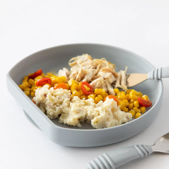 Close-up of Bumkins Silicone Grip Plate: Gray filled with chicken, corn, and potatoes on a white background.; a gray fork and spoon nearby.