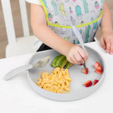 Close-up of a child enjoying macaroni, strawberries, & avocado with a fork from Bumkins Silicone Grip Plate: Gray on a white table.
