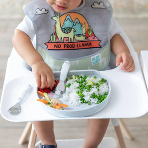 A baby wearing a llama bib in a high chair enjoys rice with peas from a Bumkins Silicone Grip Plate: Marble.