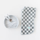 Toddler utensils rest inside Bumkins Silicone Grip Plate: Marble next to a folded gray & white checkered bib on a white background.