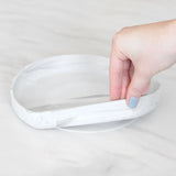 A hand holds a Bumkins Silicone Grip Plate: Marble, demonstrating the suction cup bottom on a marble surface.