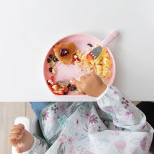 Load image into Gallery viewer, Top-down view of a child enjoying fruit, eggs, and toast from a Bumkins Silicone Grip Plate: Pink, wearing a floral bib at a white table.
