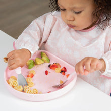 Load image into Gallery viewer, A toddler enjoys pasta, avocado, and strawberries with a fork &amp; spoon from a Bumkins Silicone Grip Plate: Pink on a white table.
