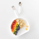 Rainbow-colored food on Bumkins Silicone Grip Plate: Vanilla Sprinkle next to matching utensils on a white background.