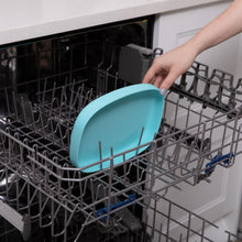 Load image into Gallery viewer, A hand places a Bumkins Silicone Grip Tray: Blue into the top rack of an open dishwasher.
