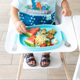 A toddler in a high chair enjoys a meal from a Bumkins Silicone Grip Tray: Blue, featuring watermelon, noodles, and star-shaped treats.
