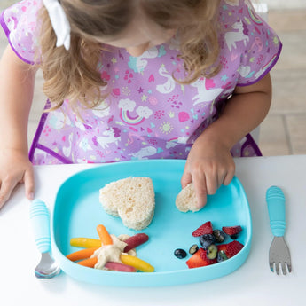 A child enjoys heart-shaped sandwiches with fruits and veggies from a Bumkins Silicone Grip Tray: Blue at a white table.