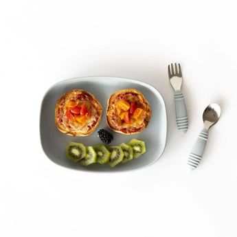 Bumkins Silicone Grip Tray: Gray holds two mini pizzas, garnished with kiwi slices and a blackberry on a white background next to utensils.
