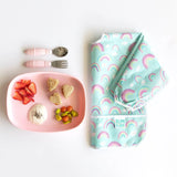 Bumkins Silicone Grip Tray: Pink with fruit and yogurt sits next to pink utensils and a folded rainbow-print bib on a white background.