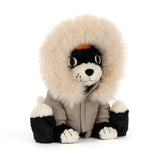 A black and white Jellycat Jack Alpine Outfit plush dog wearing a tan winter coat with a faux fur-trimmed hood.