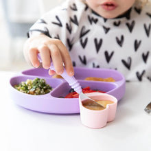Load image into Gallery viewer, A child dips a spoon in a pink Bumkins Silicone Little Dipper 3-Pack: Lollipop attached to a purple sectioned plate of food at a table.
