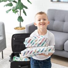 Load image into Gallery viewer, A child holds Bumkins Packing Cube 2 Pack: Mickey &amp; Friends Varsity, standing by an open suitcase in a bright room with a gray couch.
