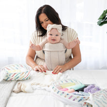 Load image into Gallery viewer, A woman wearing a smiling baby in a carrier folds clothes on a bed to pack into Bumkins Packing Cube 2 Pack: Mickey &amp; Friends Varsity.

