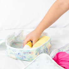 Load image into Gallery viewer, A hand places a rolled yellow shirt into a Bumkins Packing Cube 2 Pack: Aloha Stitch on a white bed.
