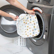 Load image into Gallery viewer, A person holds a Bumkins Packing Cube 2 Pack: Winnie + Friends in front of a front-loading washing machine.
