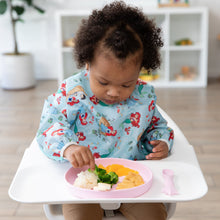 Load image into Gallery viewer, A toddler in a bib sits in a high chair, eating from Bumkins Silicone Plate + Spoon Set: Disney Princess with veggies, nuggets, and potatoes.
