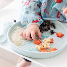 Load image into Gallery viewer, Close-up of a child in a blue bib eating fruit, rice, &amp; beans from Bumkins Silicone Plate + Spoon Set: Disney Princess Ariel.
