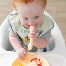 Load image into Gallery viewer, A red-haired baby in a high chair with a bib enjoys bananas and strawberries from Bumkins Silicone Plate + Spoon Set: Disney Winnie the Pooh.
