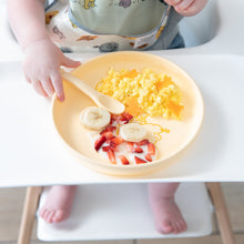 Load image into Gallery viewer, A toddler enjoys breakfast from a Bumkins Silicone Plate + Spoon Set: Disney Winnie the Pooh on a high chair's white tray.

