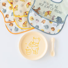 Load image into Gallery viewer, Bumkins Silicone Plate + Spoon Set: Disney Winnie the Pooh lays on a white background next to three waterproof bibs.
