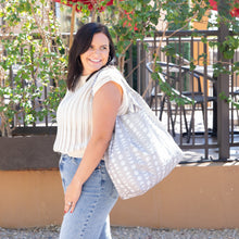 Load image into Gallery viewer, A woman with long dark hair smiles outdoors, wearing a white top and jeans, carrying a Bumkins Packable Tote Bag: Lunar Phase.
