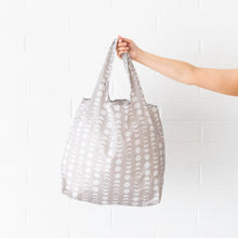Load image into Gallery viewer, Someone holds the Bumkins Packable Tote Bag: Lunar Phase against a white brick wall.
