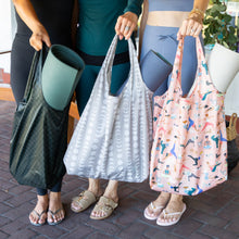 Load image into Gallery viewer, Three people stand on a brick path holding bags with yoga mats. The middle person holds the Bumkins Packable Tote Bag: Lunar Phase.
