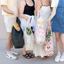 Load image into Gallery viewer, Four people hold bags filled with groceries against a light background. One holds Bumkins Packable Tote Bag: Boots filled with popcorn.
