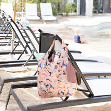 Load image into Gallery viewer, Beach chairs by a pool with a Bumkins Packable Tote Bag: Yoga Pals hanging on one. A child plays near the water in the background.

