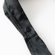 Load image into Gallery viewer, Close-up of the Bumkins Packable Tote Bag: Rich Black on a white background, showcasing the snap button closure on the straps.
