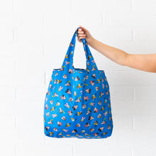 Load image into Gallery viewer, A hand holds a Bumkins Packable Tote Bag: Mickey &amp; Friends Forever against a white brick wall.
