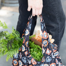Load image into Gallery viewer, A person holds a Bumkins Packable Tote Bag: Ghostly Gallery with fresh greens, featuring a Nightmare Before Christmas design.
