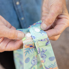 Load image into Gallery viewer, Close-up of hands snapping shut a strap on the Bumkins Packable Tote Bag: Aloha Stitch.
