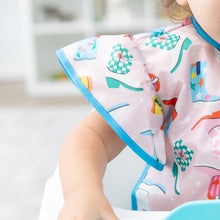 Load image into Gallery viewer, Close-up of a child wearing a Bumkins Ruffle Apron Bib: Boots in a high chair, with focus on the bib's ruffle sleeve.
