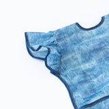 Close-up of Bumkins Ruffle Apron Bib: Crushed Denim on a white background, with focus on the ruffle sleeve.