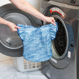 A person holds Bumkins Ruffle Apron Bib: Crushed Denim in front of an open front-loading dishwasher.